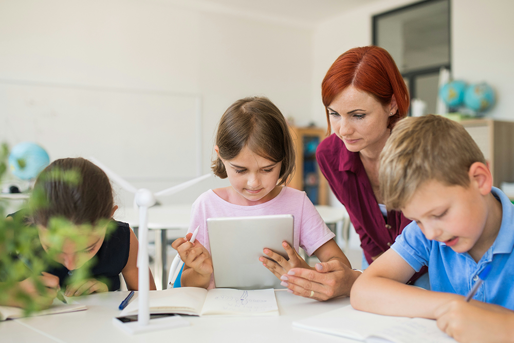 Photo of a primary school student working on her iPad in class with her teacher.